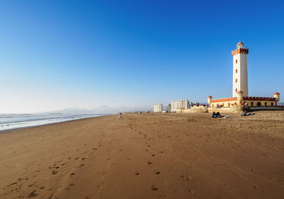 Lighthouse on beach by sea against clear sky