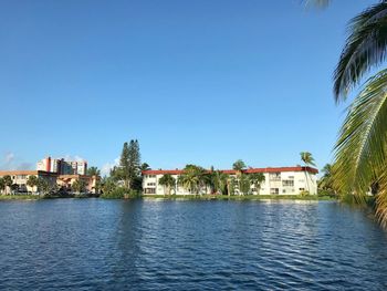 Buildings by lake against blue sky