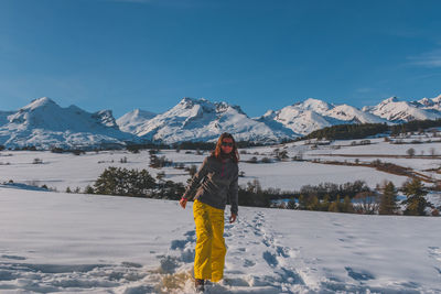 A full-body shot of a young caucasian woman standing in the french alps mountains in la joue du loup