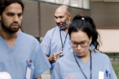 Mature nurse gesturing while talking to colleague outside hospital