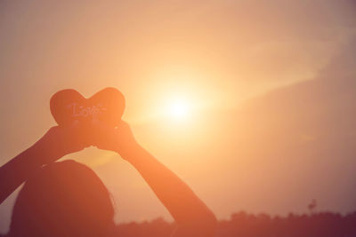 Silhouette person holding heart shape against sky during sunset