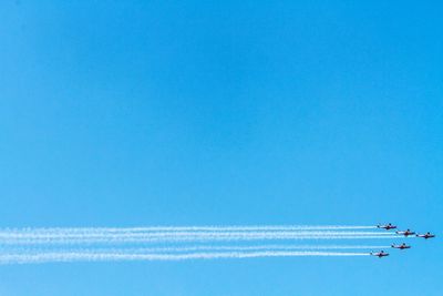 Low angle view of airplanes flying against clear blue sky