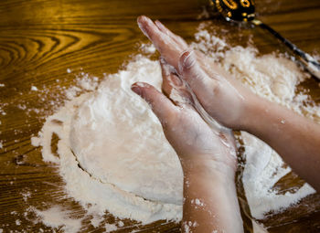 Cropped hands on kid flattening dough on table