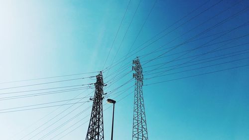 Low angle view of electricity pylon against blue sky