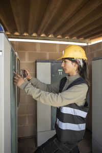 Female maintenance engineer comparing circuit board with smart phone at power station