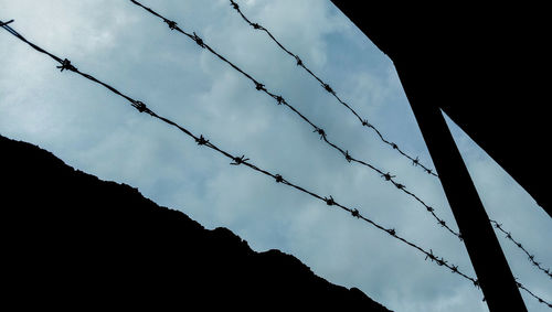 Low angle view of silhouette barbed wire fence against sky