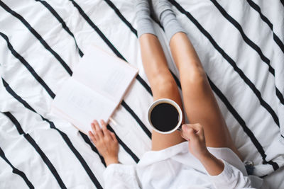 Midsection of woman holding coffee cup on bed