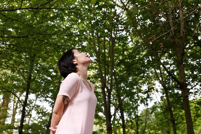 Low angle view of woman standing against trees in forest