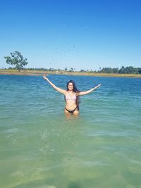 Woman wearing bikini while standing in sea against clear blue sky