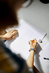 Anonymous creative woman standing at table with sketch and pencil while working on project