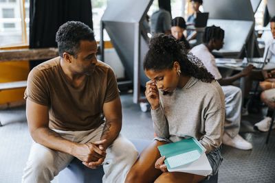 Male professor talking with stressed teenage girl while sitting in cafeteria at school