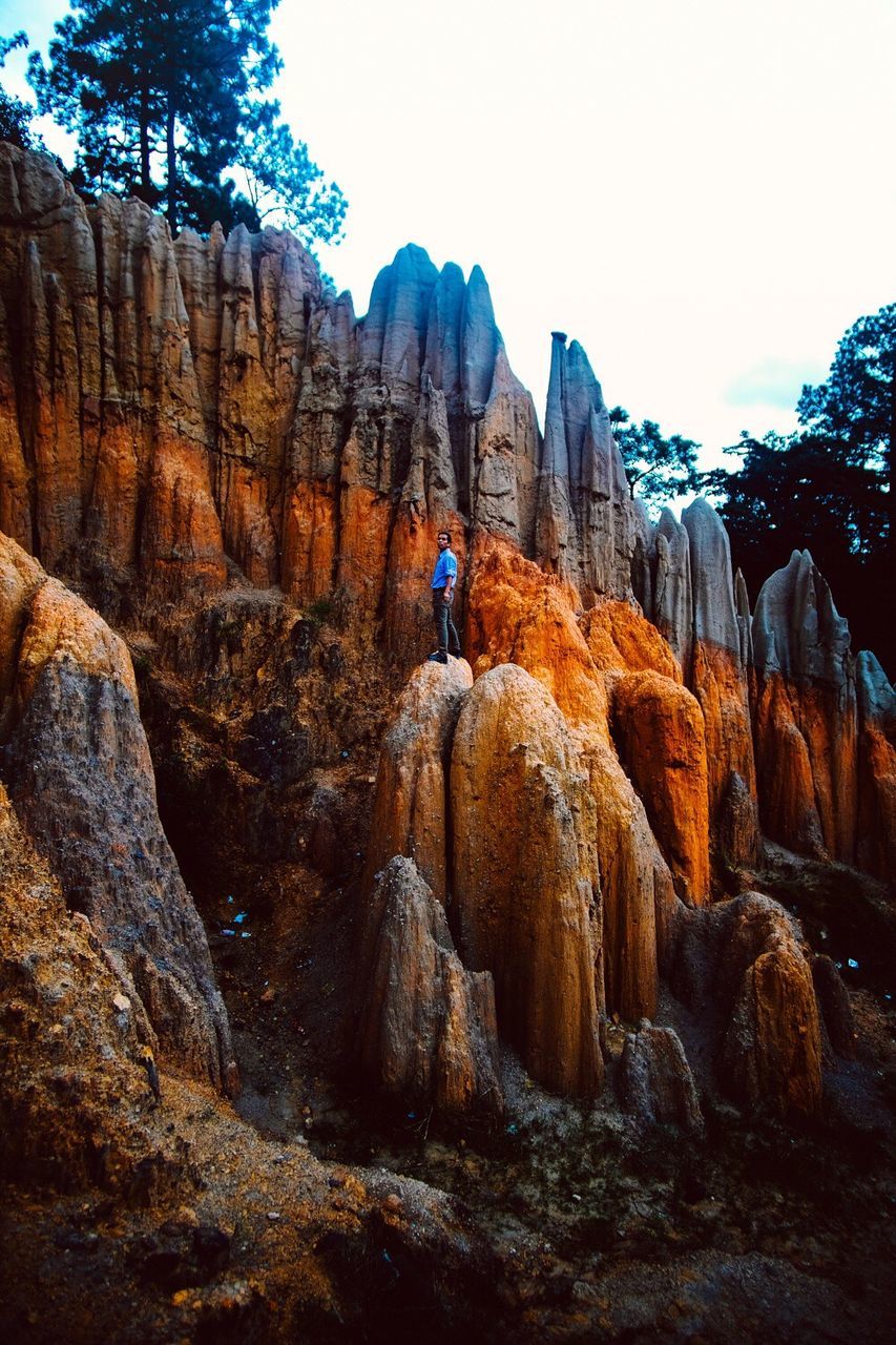 rock - object, nature, leisure activity, adventure, day, cliff, outdoors, one person, travel, mountain, beauty in nature, landscape, challenge, low angle view, lifestyles, scenics, real people, clear sky, full length, climbing, tree, young adult, sky, adult, people