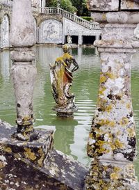 Statue by lake against stone wall