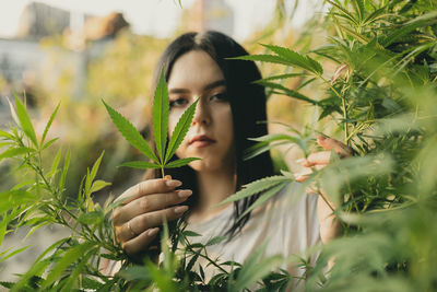 Portrait of young woman holding leaf of cannabis plant