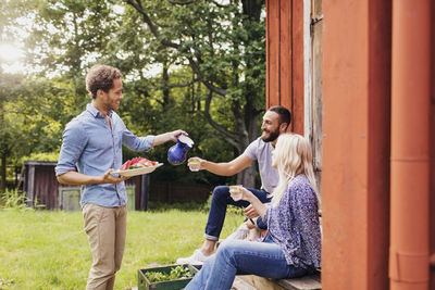 Man holding salad tray while serving drink to friends