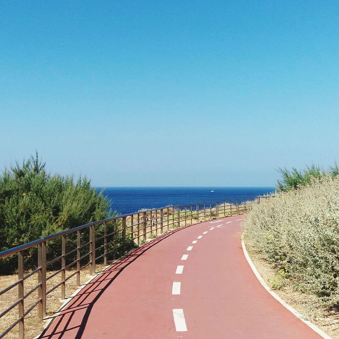 sea, horizon over water, clear sky, blue, road, the way forward, copy space, empty, water, tranquil scene, road marking, ocean, transportation, tranquility, railing, long, coastal road, day, scenics, solitude, yellow line, white line, outdoors, narrow, surface level, tourism, dividing line, remote, curve, beauty in nature