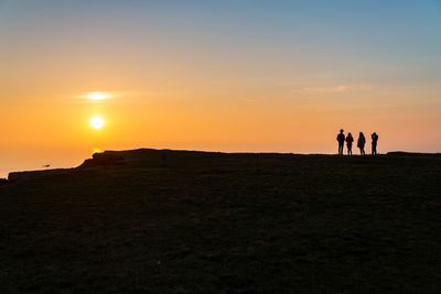 Silhouette men on landscape against sky during sunset