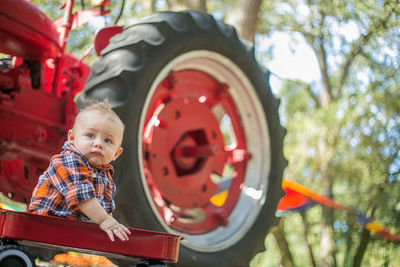 Baby boy looking away while sitting on cart against tractor