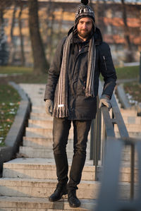 Portrait of young man in warm clothing moving down on steps at park