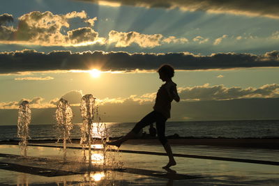 Side view of young woman playing with fountain at beach