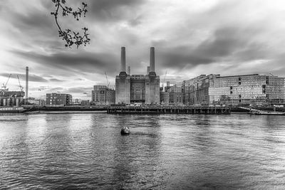 Buildings by river against cloudy sky