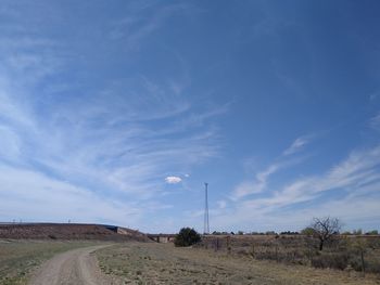 Road amidst field against blue sky