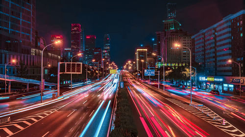 Light trails on city street amidst buildings at night