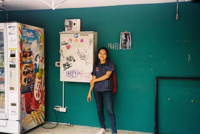 Portrait of smiling young woman standing against wall