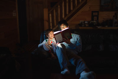 A happy boy listens to his father read book in early morning on couch