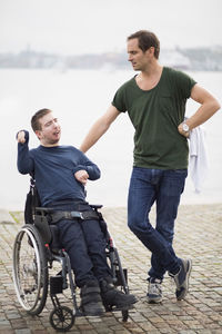 Disabled man on wheelchair taking with male caretaker by lake