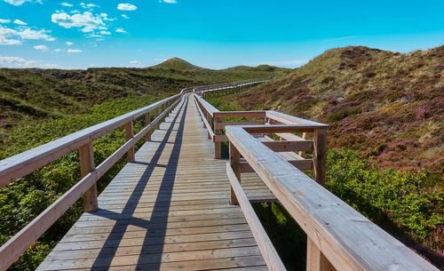 Footbridge leading towards mountains against sky