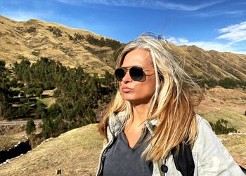 Portrait of young woman wearing sunglasses standing on mountain against sky