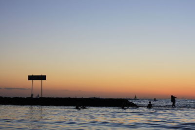 Silhouette man by sea against clear sky during sunset