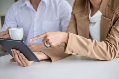 Midsection of businesswoman showing digital tablet to colleague