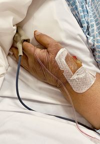 Cropped hand of woman with iv drip on bed