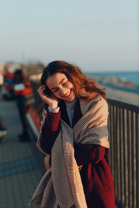 Smiling young woman standing by railing against sky during winter