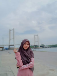 Young woman wearing hijab standing against bridge