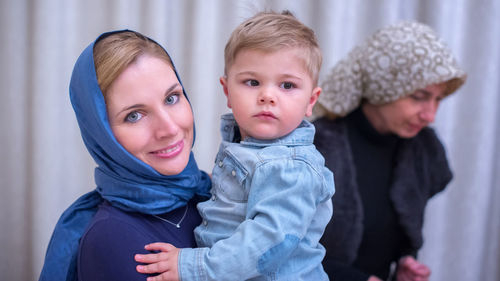 Portrait of mother carrying son while standing at home