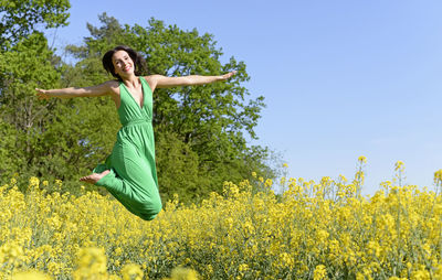 Portrait of smiling young woman jumping at oilseed rape field