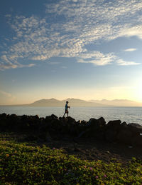 Silhouette man standing at beach against sky during sunset