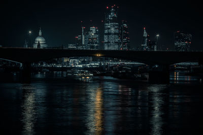 Illuminated buildings by river against sky at night