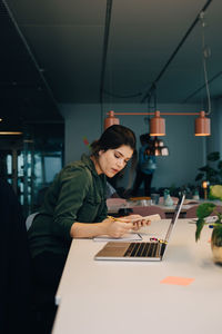 Side view of businesswoman using smart phone while working at desk in creative office
