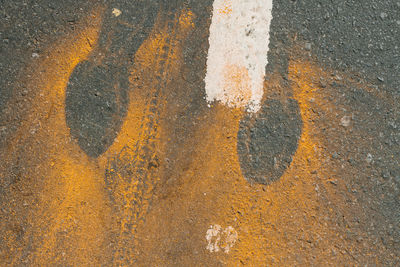 Directly above shot of footprints made by yellow powder paint on road