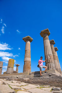 Low angle view of man standing by old ruin against blue sky