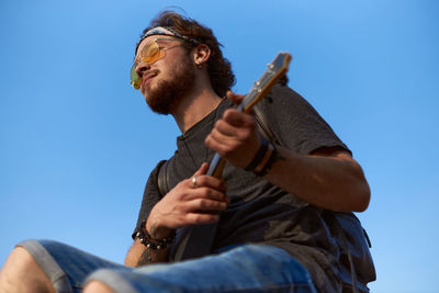 Low angle view of young man holding camera against clear sky