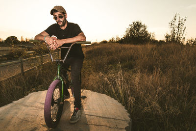 Portrait of man riding bicycle on field during sunset