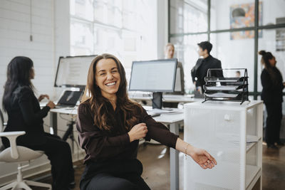 Happy businesswoman pulling sleeve while sitting at office