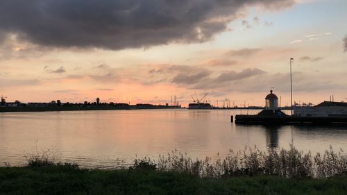 Scenic view of river by buildings against sky during sunset