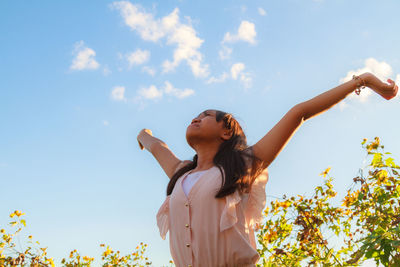 Low angle view of young girl with arms outstretched standing against sky