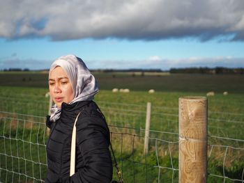 Woman looking away while standing by railing against sky